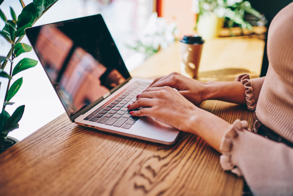 From above of crop female in casual clothes creating freelance project working on laptop typing on computer sitting at table in cafe